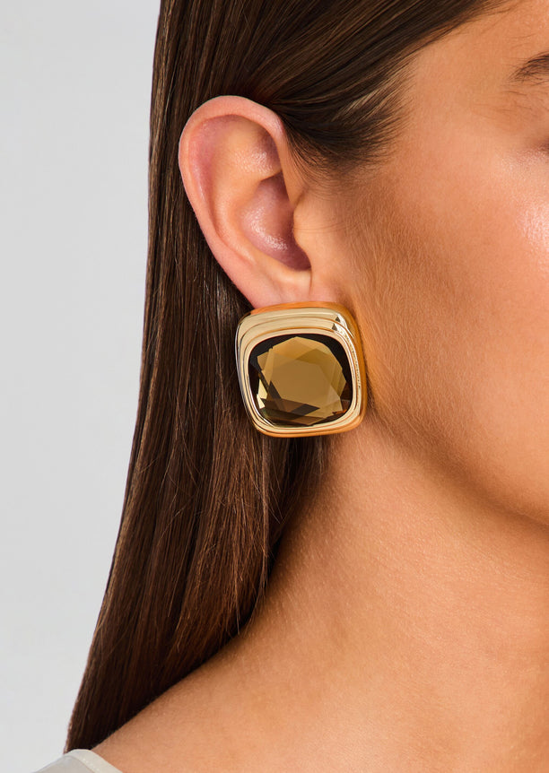 Close-up of ear wearing a Clive Earring with a square brown gemstone in a bold gold-tone setting.