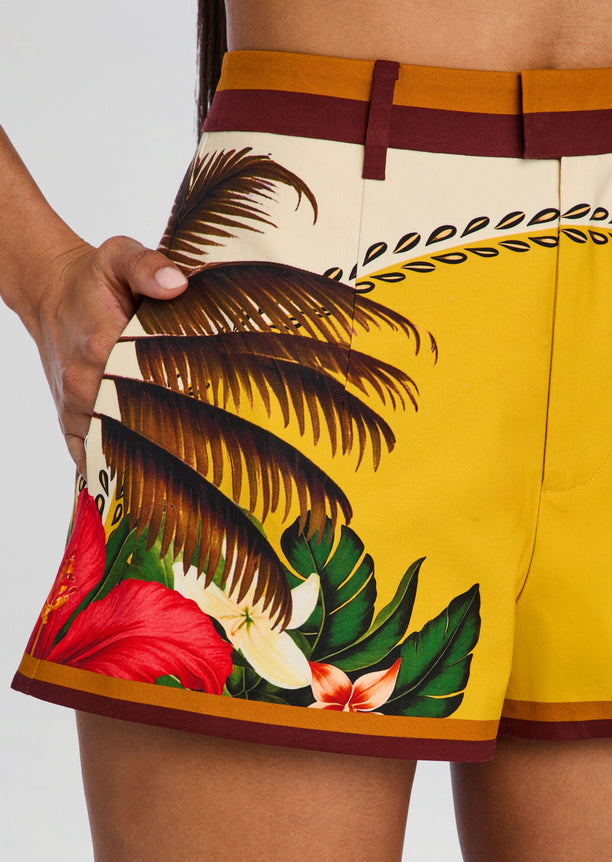 Close up of Tansie Short showing tropical palm leaf print on yellow fabric with brown trim.