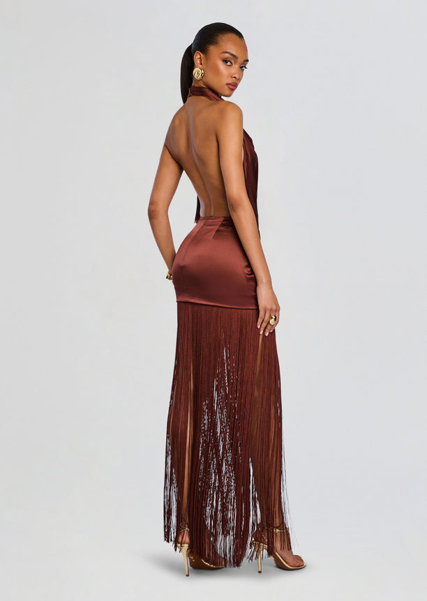 Back view of a model wearing a bronze satin halter dress with an open back and a long fringe skirt.