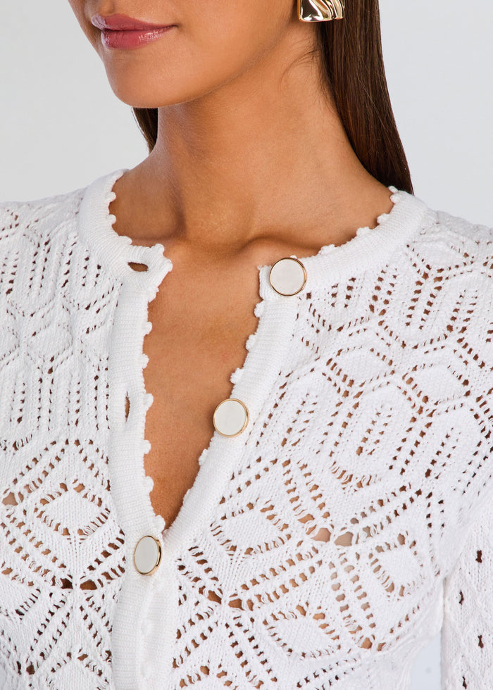 Close up of the cardigan neckline showing round white buttons with gold trim and a scalloped edge. media 3 of 5