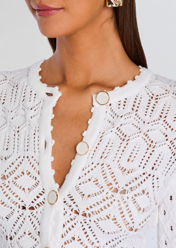 Close up of the cardigan neckline showing round white buttons with gold trim and a scalloped edge.