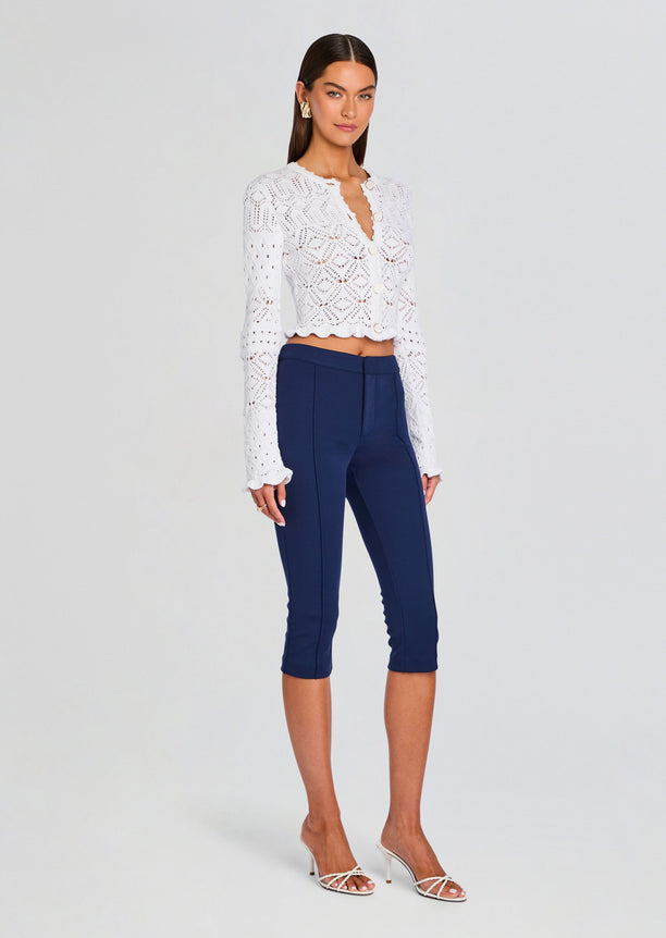 White Giuliana Crochet Cardigan with scalloped hem and round buttons, styled with navy cropped pants.