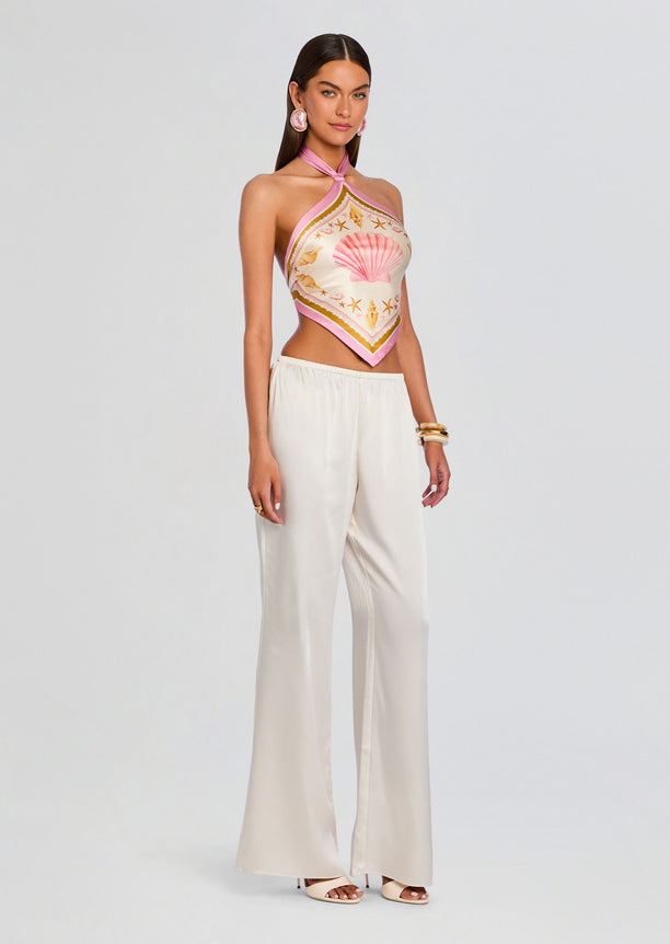 Model wearing Jamie Silk Top with pink halter tie and seashell print, paired with cream wide-legged pants.
