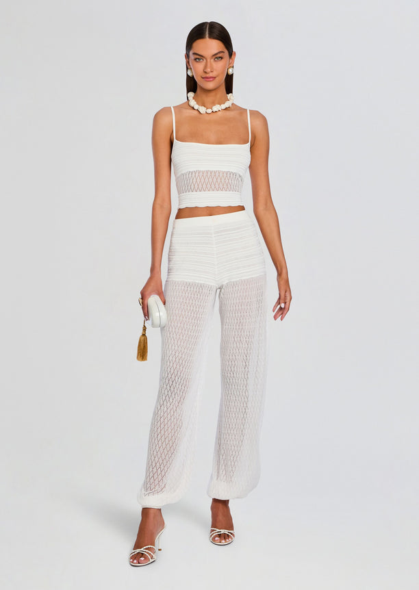 Model wearing a white crochet crop top and matching lattice-pattern pants from the Devyn Pant set with white sandals