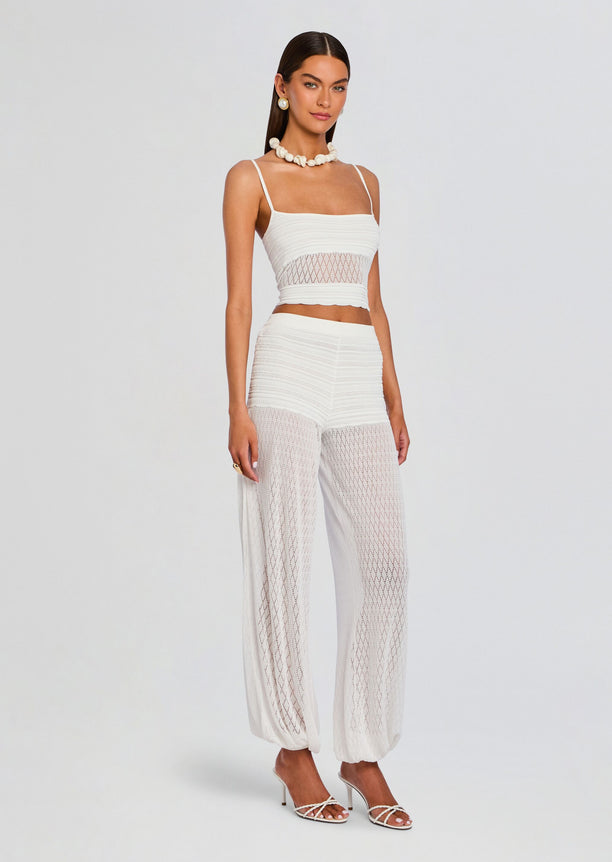 Model wearing white Devyn Pant set with a high waist knit top and sheer lattice panels along the legs.