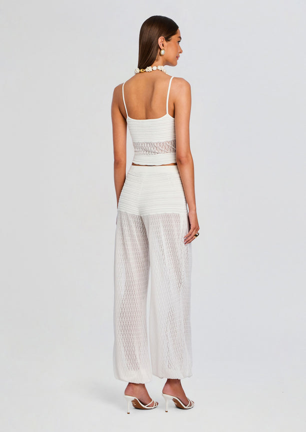 Rear view of a model in white Devyn Pant set showing lattice sheer legs and a cropped top with strappy heels.