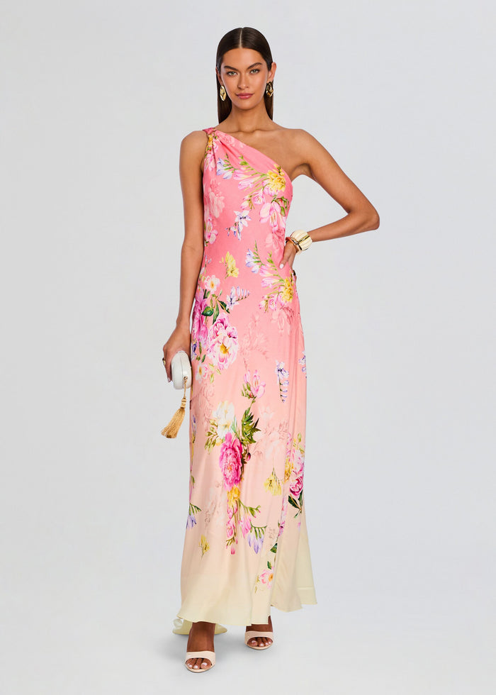 Full-length pink floral Avya one-shoulder sash dress on a model, holding a white tassel clutch. media 1 of 5