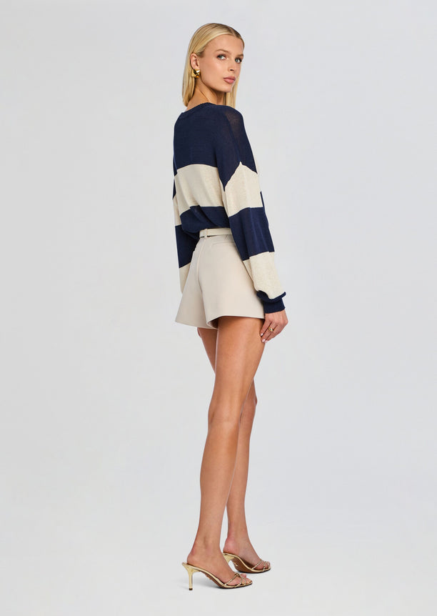 Model in a navy and cream striped Cassian Sweater paired with beige high waisted shorts and gold heeled sandals.