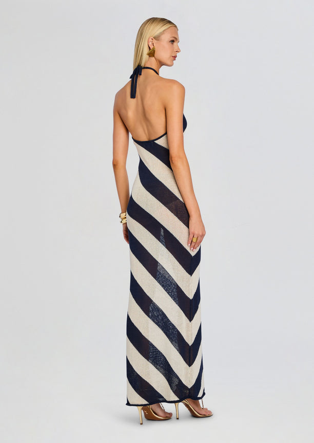 Back view of a model wearing a halter neck knit maxi dress with navy and beige diagonal stripes and an open back