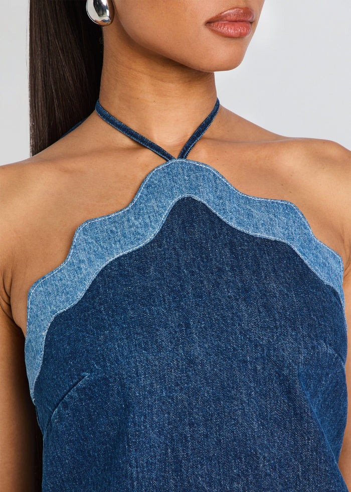 Close-up of a model wearing a halter top made of layered denim fabrics in dark and light blue, featuring a scalloped edge and thin neck straps. media 2 of 5