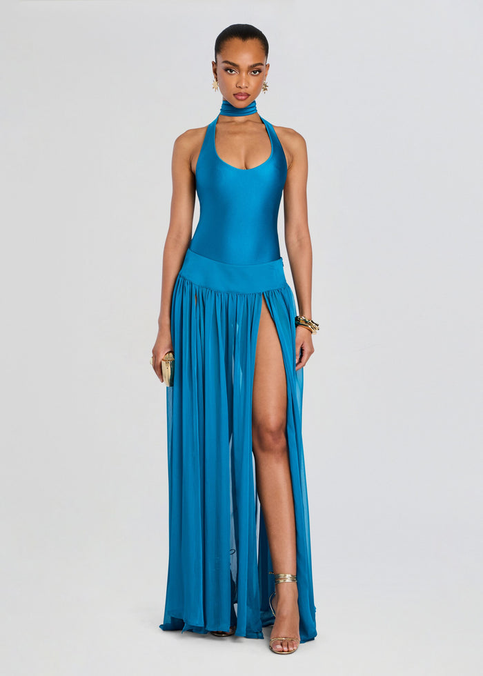 Woman wearing a blue halter neck dress with a slit on a light gray background media 2 of 5