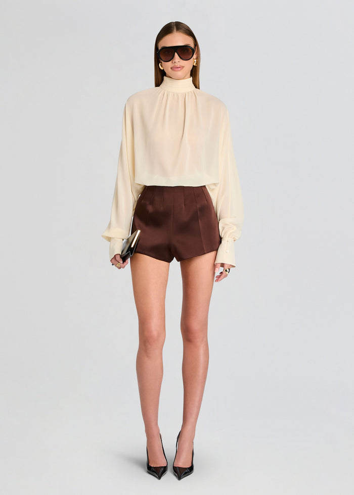 Woman wearing a beige blouse and brown shorts on a light gray background media 2 of 5