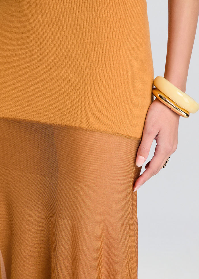 Close-up of a person wearing a mustard yellow dress with a gold bracelet on a light gray background media 2 of 5