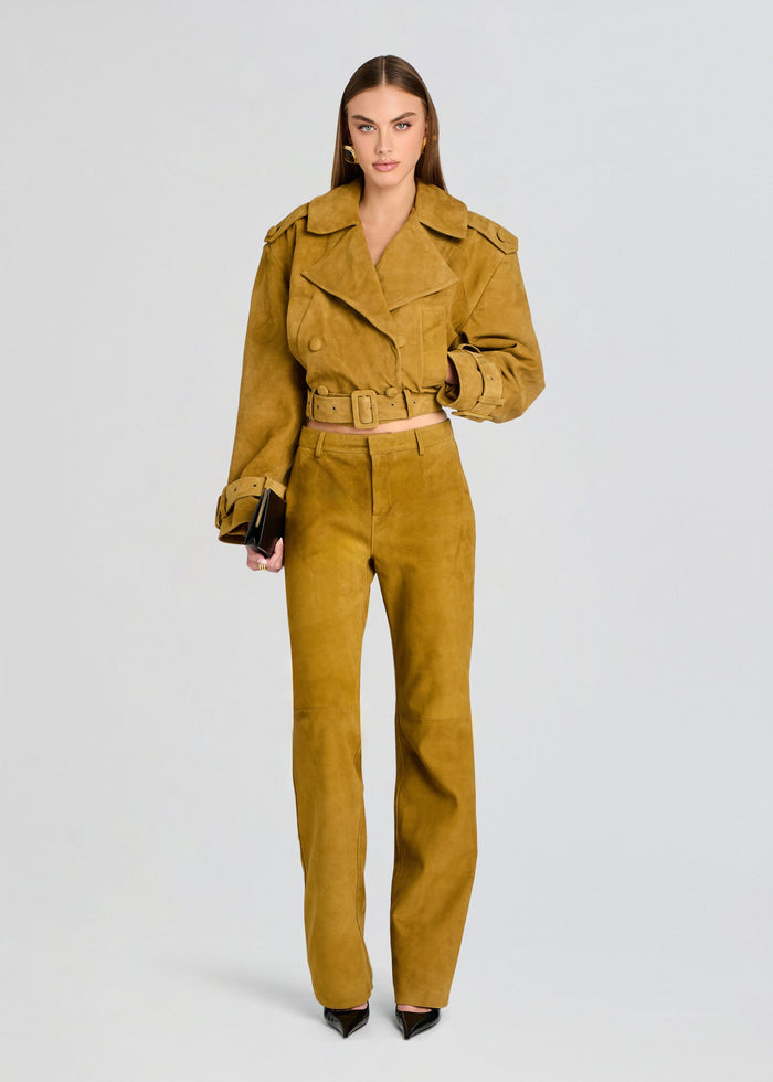 A model wearing a matching mustard yellow suede jacket and wide-leg trousers set, styled with black pointed-toe heels and a small black clutch, against a light gray studio background. media 2 of 5