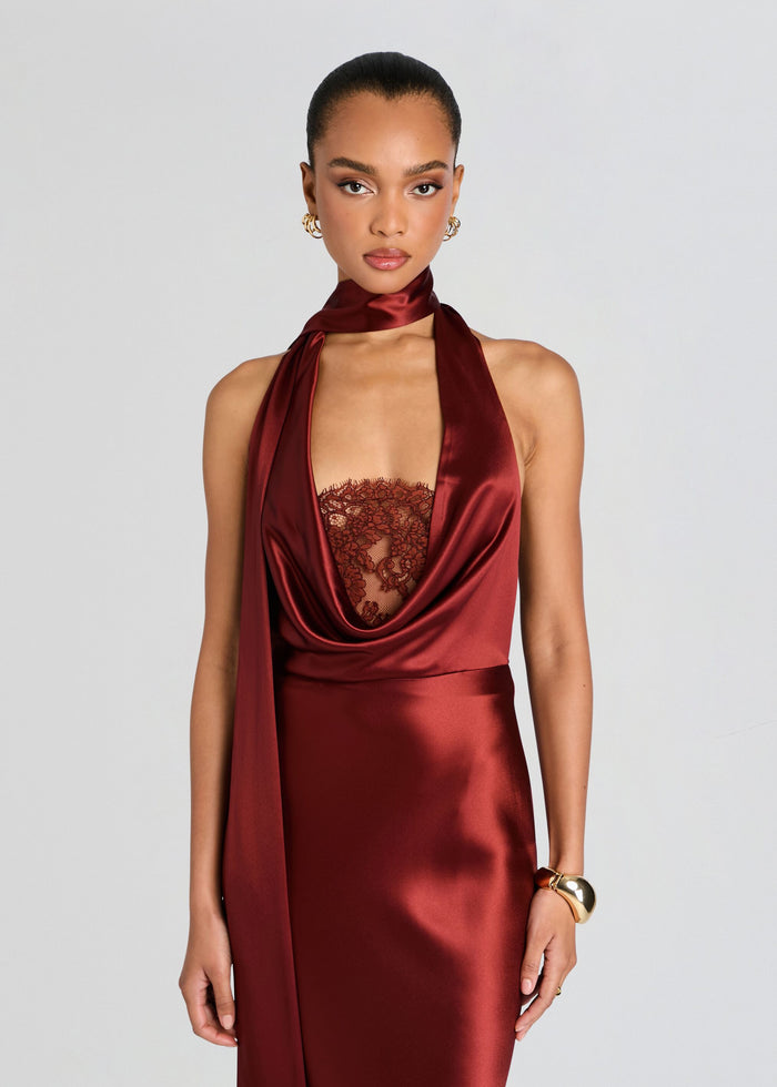 A model wearing a deep burgundy satin halter dress with a sheer lace corset-style bodice and a matching satin neck drape, set against a solid light gray background. media 5 of 5