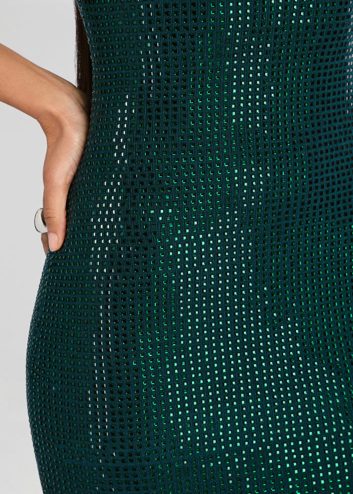 Close-up of a dark green bodycon dress with a textured, perforated mesh pattern, worn by a model whose hand is visible on the left side. media 2 of 5