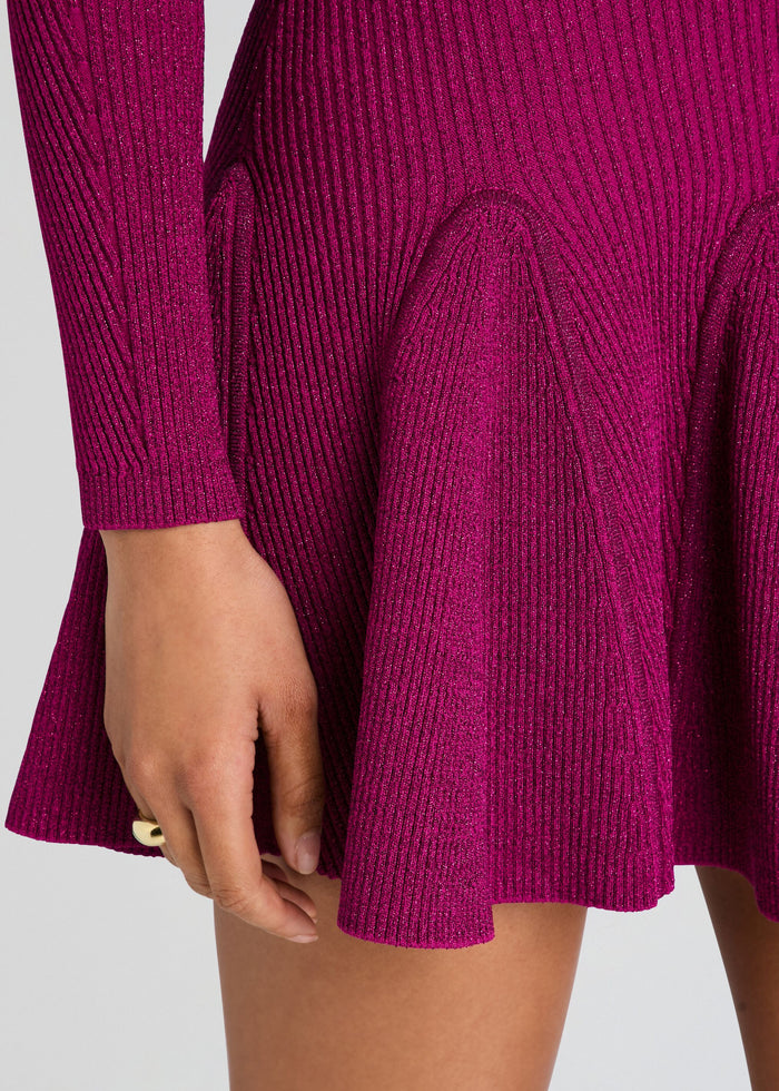 Close-up of a ribbed knit long-sleeve dress in a rich magenta-purple color, featuring a flared skirt and a hand resting near the hem. media 2 of 5