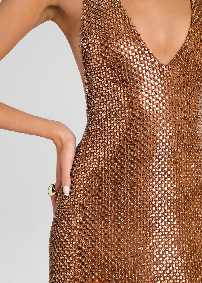 Close-up of a model wearing a bronze metallic mesh dress with a deep V-neckline and side pockets, set against a plain light gray background. media 2 of 5