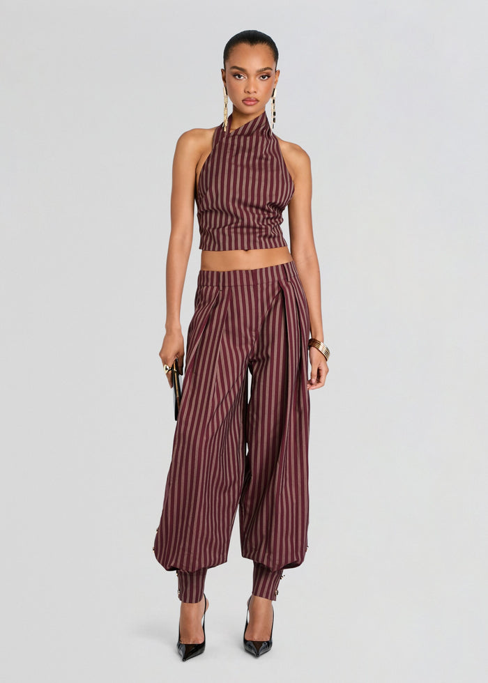 A model wearing a matching two-piece set consisting of a halter crop top and high-waisted wide-leg pants, both in a dark burgundy and black vertical stripe pattern, set against a plain light gray studio background. media 2 of 5