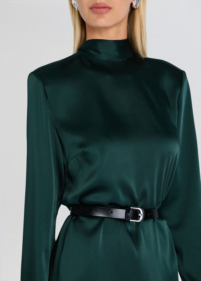 A close-up of a model wearing a dark green satin long-sleeve dress with a high mock neck and a black belt with a silver buckle at the waist. media 2 of 5