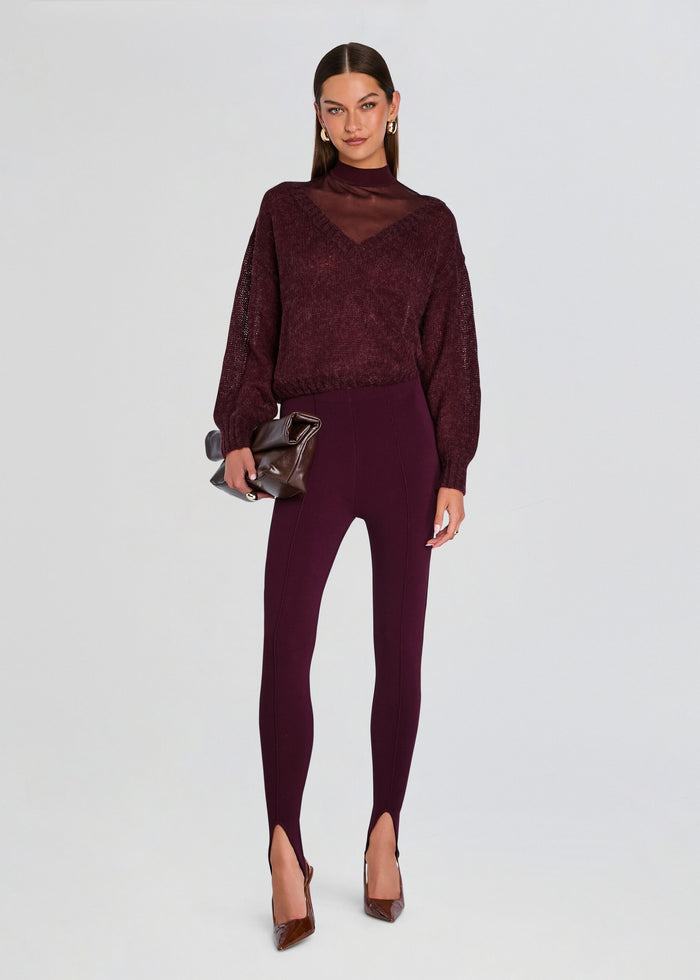 A model stands against a light gray studio background wearing a matching burgundy textured long-sleeve top and high-waisted leggings set, holding a dark metallic clutch and wearing brown pointed-toe heels. media 2 of 5