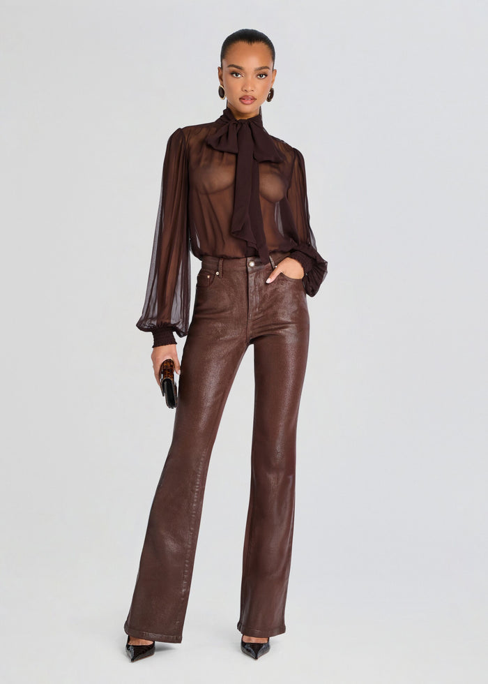 A model stands against a light gray studio background wearing a sheer dark brown long-sleeve blouse with a high neck and ruffled collar, paired with dark brown faux-leather flare pants and black pointed heels. media 2 of 5