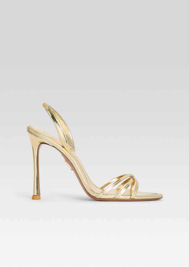 Anabel Sandal in gold metallic with slender cross straps and a tall stiletto heel seen from the side.