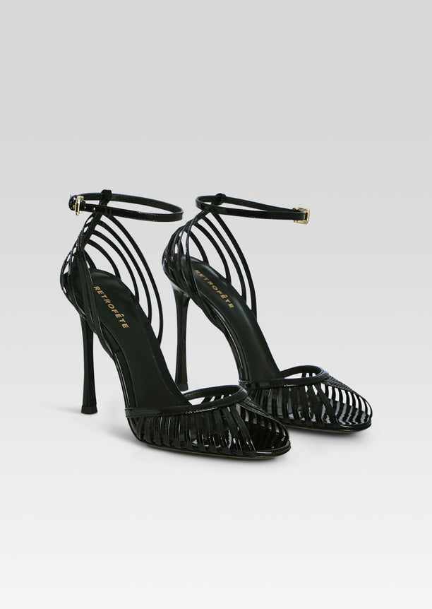 Pair of black high heel Analu Sandals with ankle straps and cage front on a light background