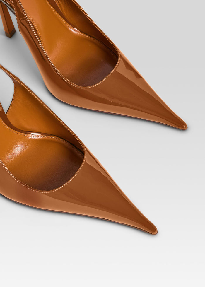 A close-up studio shot of a pair of pointed-toe slingback pumps in glossy cognac brown leather, showing the upper and heel details against a light gray background. media 3 of 5