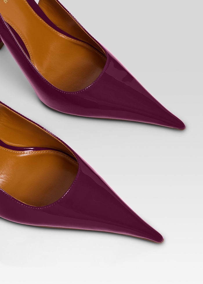 Close-up of a pair of pointed-toe high heels in glossy deep burgundy patent leather with tan interiors, shown on a light gray background. media 3 of 5