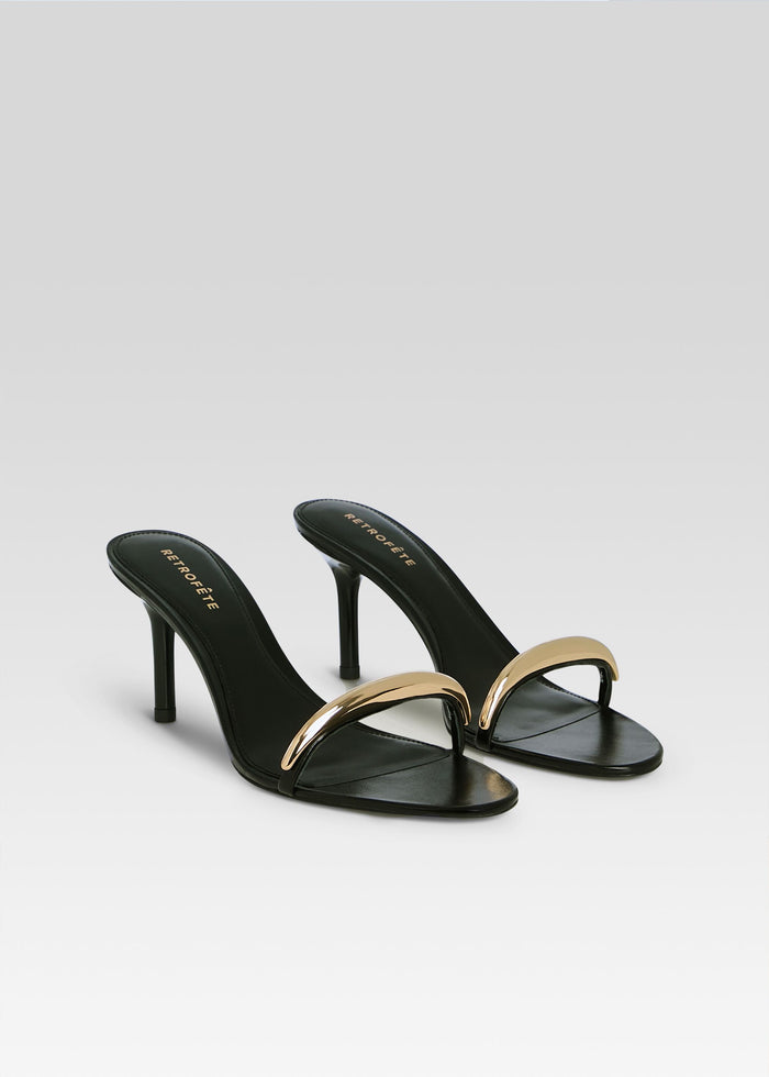 Two Karli Sandals with black leather and gold curved strap on a light gradient backdrop media 4 of 5