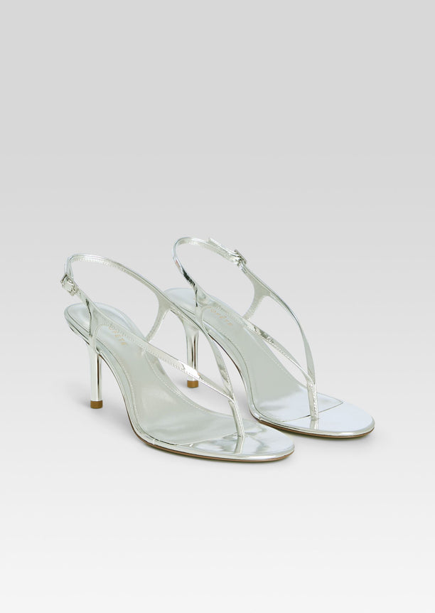 Pair of metallic silver Klotilde Sandals with slender straps and high heels on a light backdrop