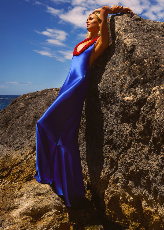 Woman in a blue dress with a red details standing on a rocky cliff with ocean view media 2 of 6
