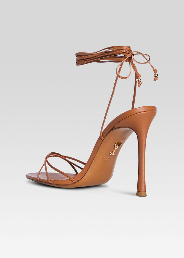 Side view of a tan strappy Lucia Sandal with a tall stiletto heel and ankle wrap media 5 of 5