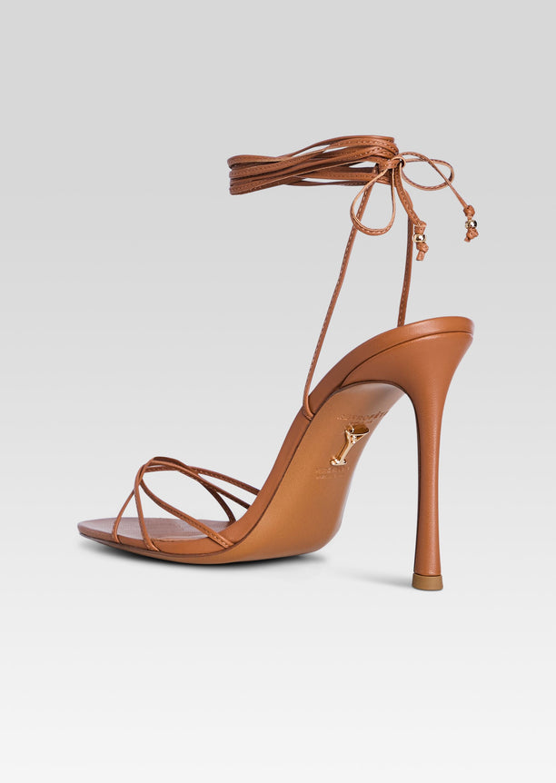 Side view of a tan strappy Lucia Sandal with a tall stiletto heel and ankle wrap