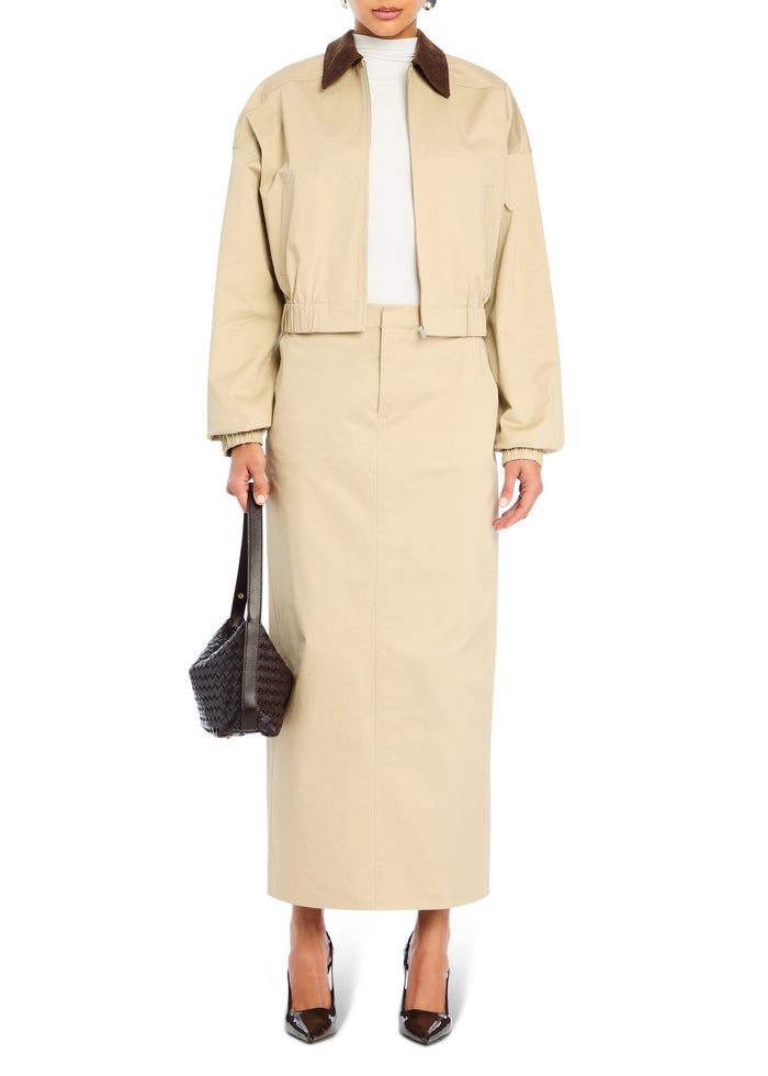 Beige cropped jacket with a brown collar worn over a white turtleneck, paired with a long beige skirt and a dark woven bag. media 5 of 5