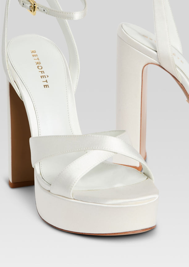 Close up of white platform sandal showing crisscross front straps and tall block heel with tan sole edge.