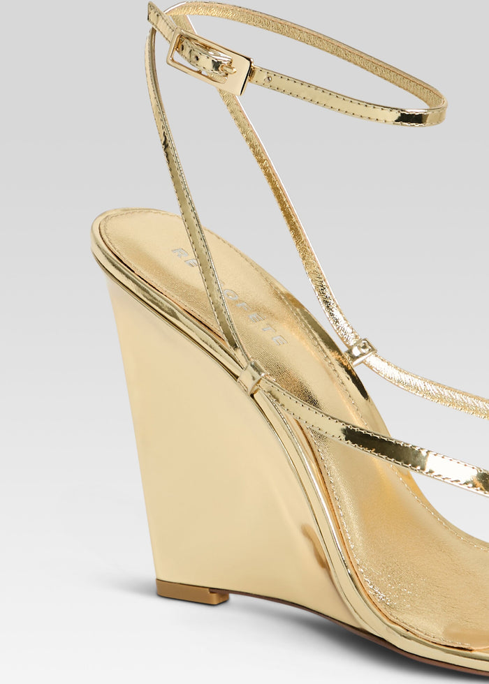 Close up of a gold metallic wedge sandal showing slim ankle strap and buckle. media 3 of 5