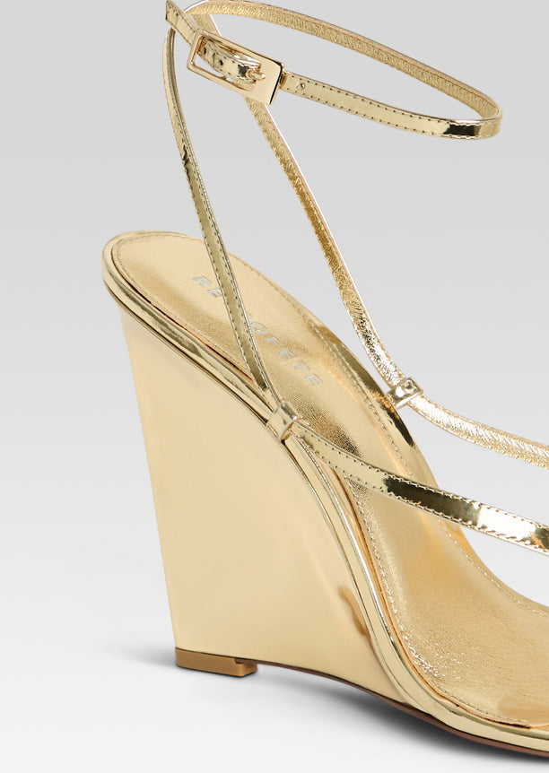 Close up of a gold metallic wedge sandal showing slim ankle strap and buckle.