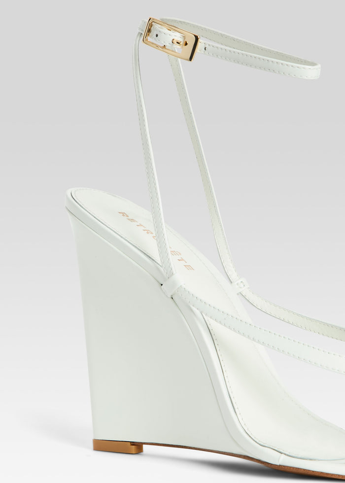 Close-up of Namby Wedge white sandal showing ankle strap with gold-tone buckle and wedge heel media 3 of 5