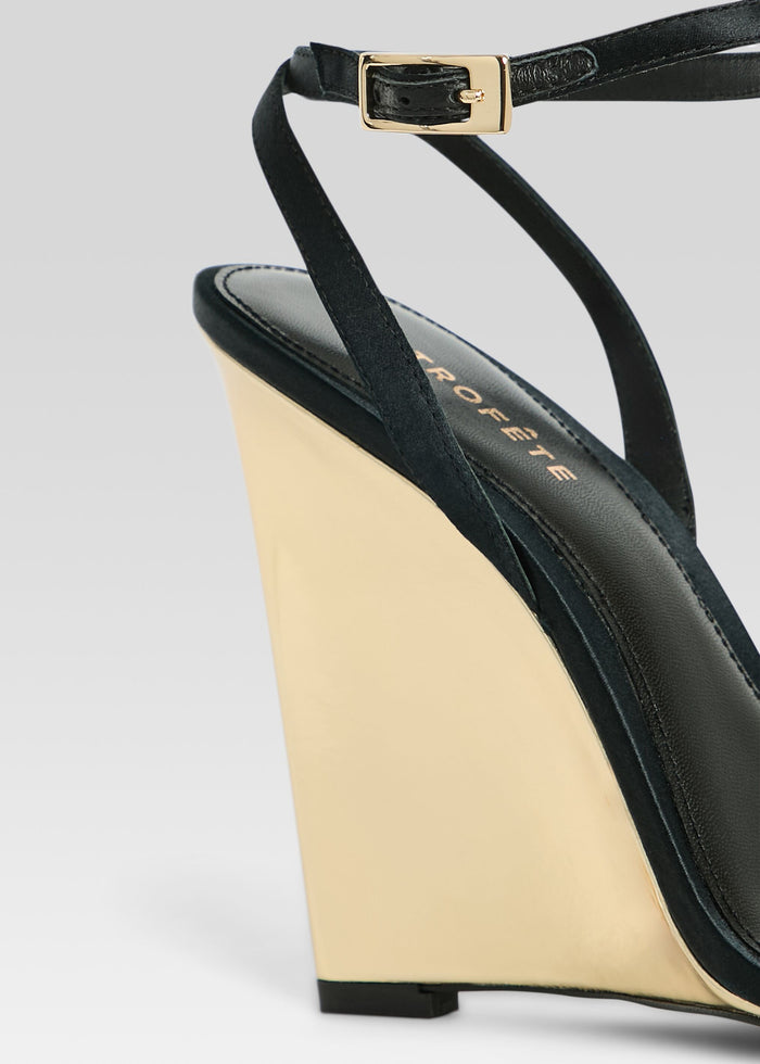 Close up of Nelly Wedge showing black ankle strap with gold buckle and gold wedge heel. media 3 of 5