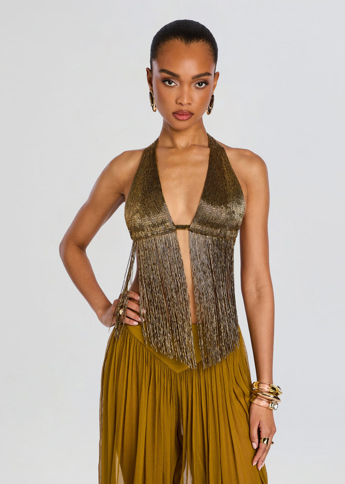 Model wearing a metallic gold embellished fringe halter top with long fringe panels and gold accessories. media 1 of 6