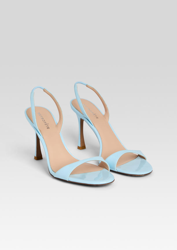 Pair of light blue Fortune Sandals with slim straps and stiletto heels on a white gradient background.