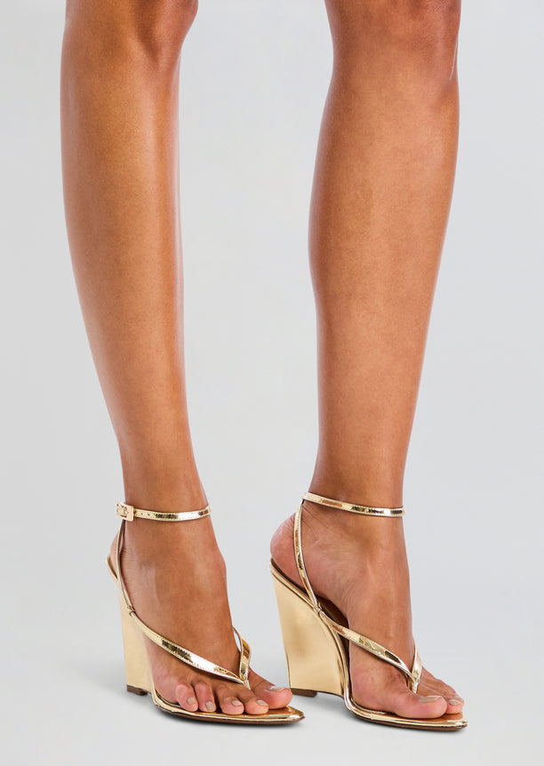 Model wearing gold metallic wedge sandals with a slim ankle strap.