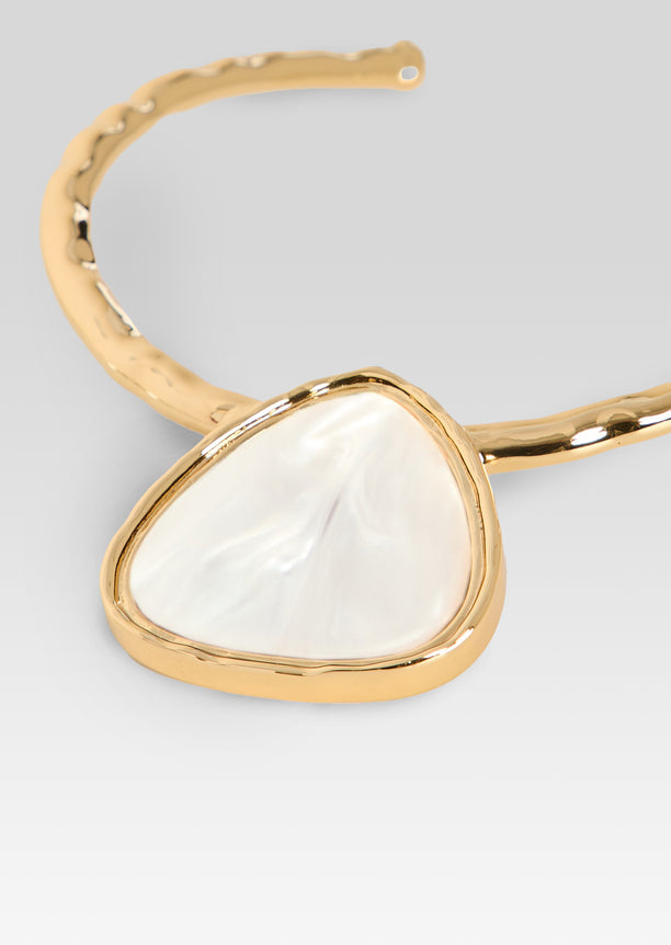 Close-up of gold necklace with triangular white pearl pendant in a rounded bezel setting