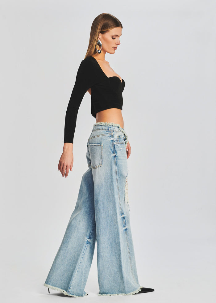 Side profile of a model wearing a black long sleeve crop top and distressed wide leg jeans. media 4 of 6