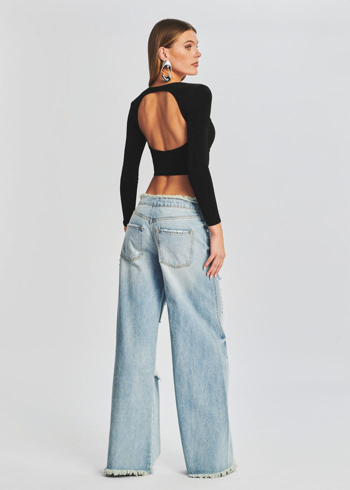 Back view of model in black long sleeve cropped top with open back, paired with distressed wide-leg jeans. media 2 of 6