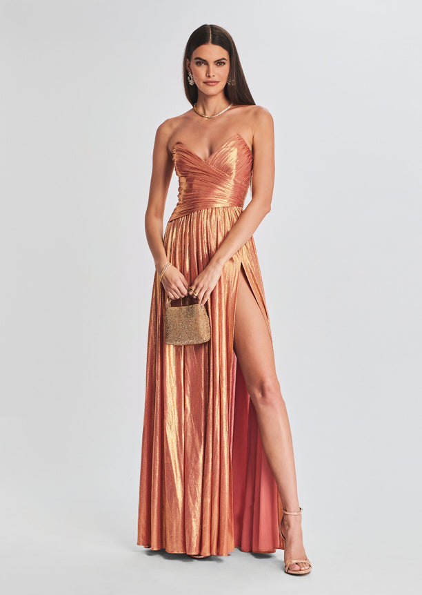 Waldorf Dress in metallic rose gold with a ruched strapless bodice and thigh-high slit, model holding a small glittery handbag.